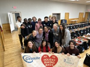 a group of high school students pose with a banner that reads "JKF Holiday Baking Bags 2022" with a large red heart 